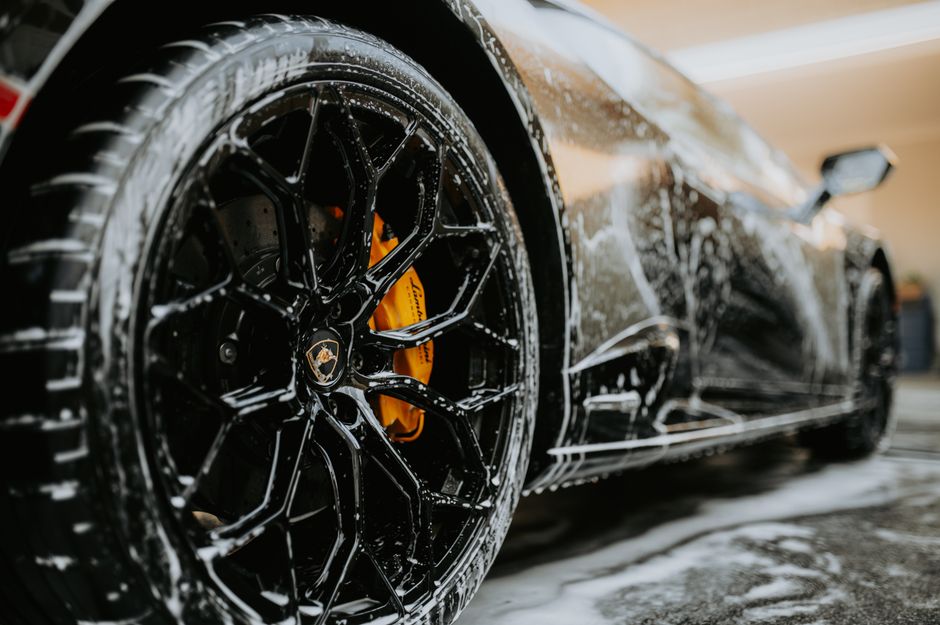 Detailer's gloved hands hand-polishing a car's black paintwork to a high-end shine
